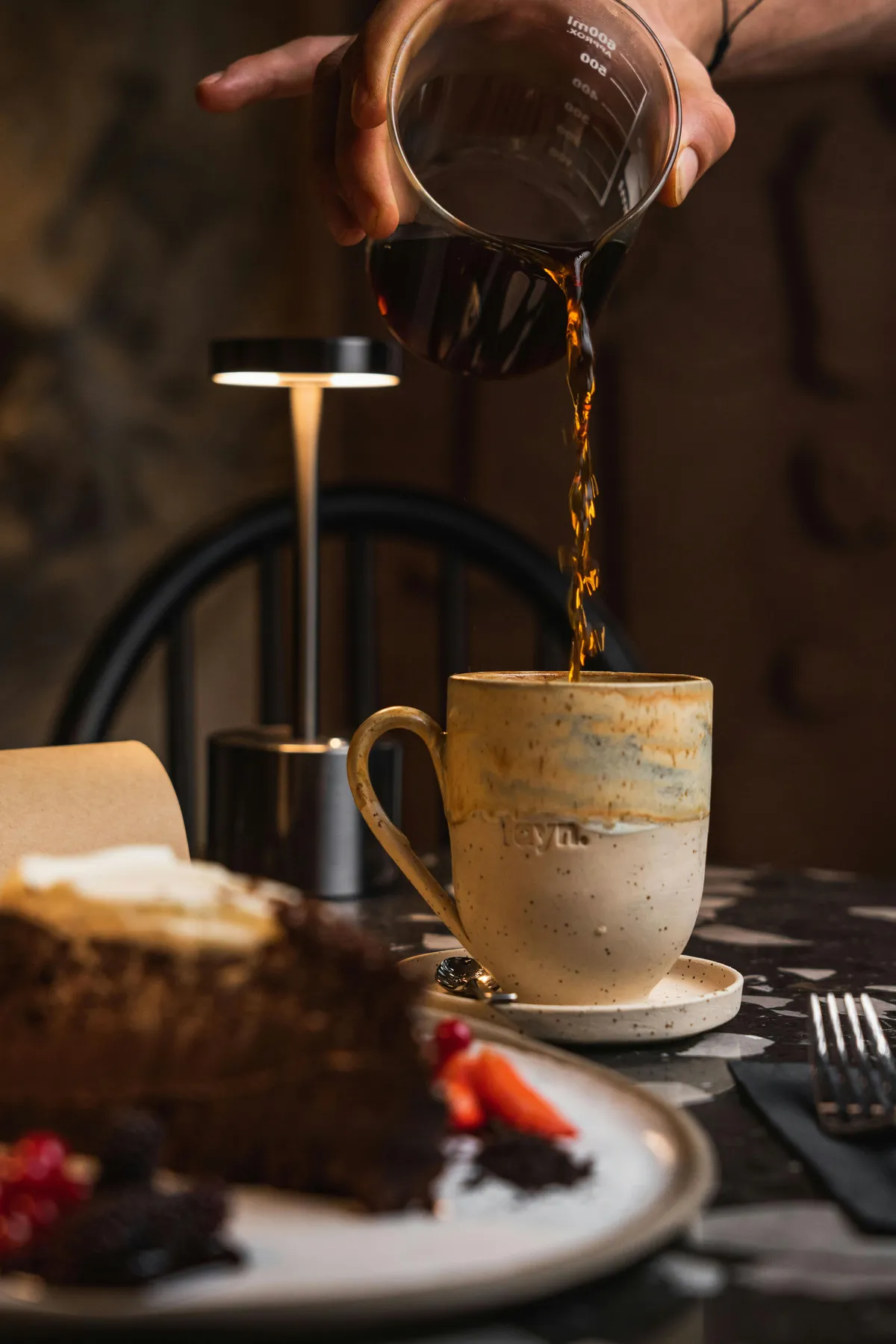 Kaffee wird aus einem Glas in eine Tasse gegossen, daneben Schokoladenkuchen