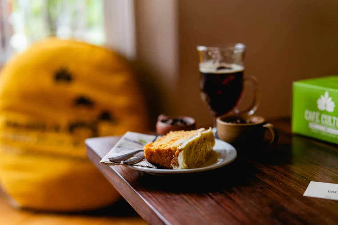 Kuchen und ein Glas Kaffee auf einem Holztisch, daneben ein gelbes Kissen